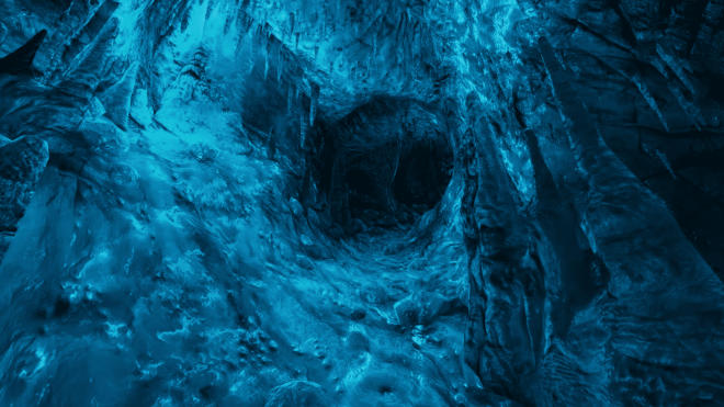 A cave tunnel whose walls have water running down them and which are bathed in blue light.